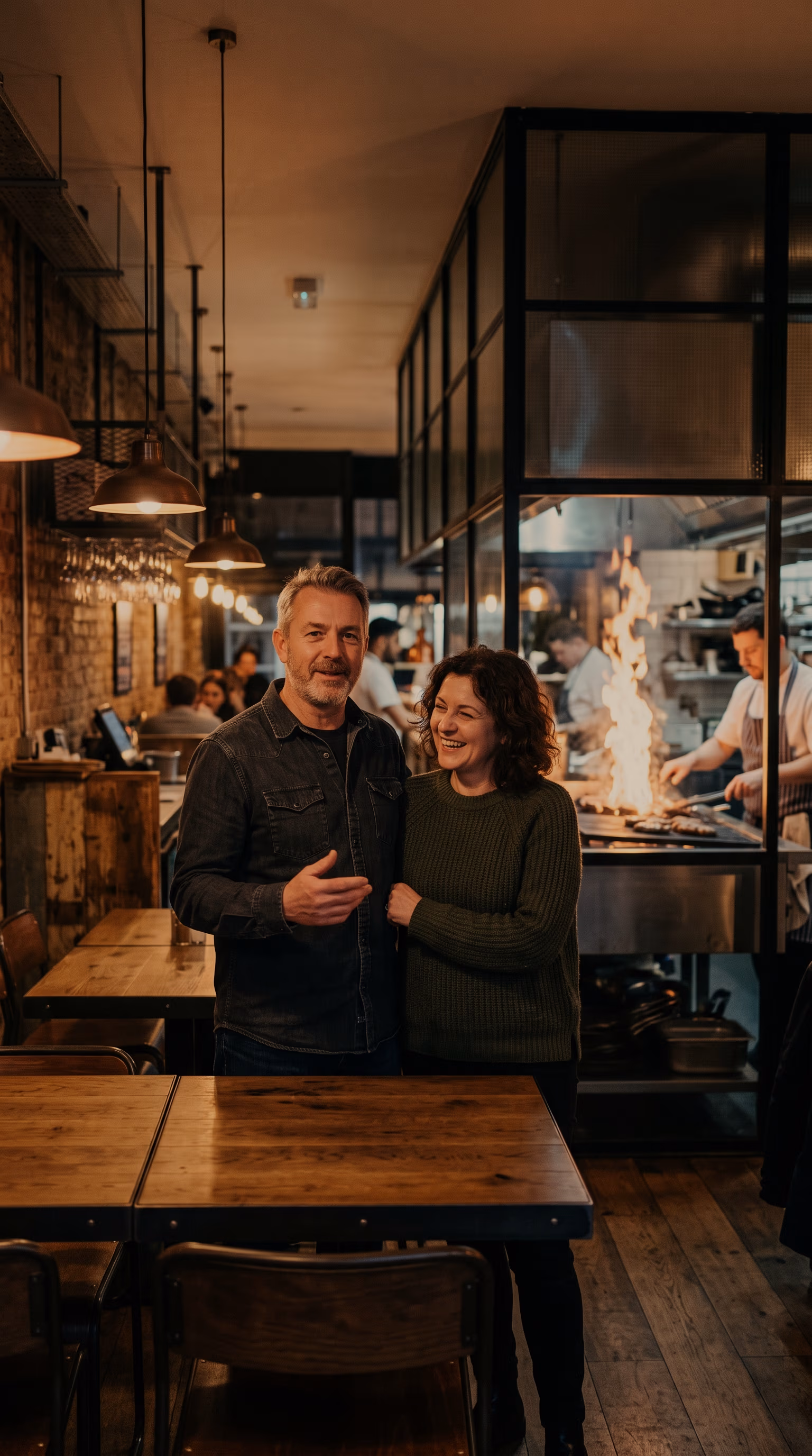 Tom and Ade Whitlock in the dining room, the open kitchen and its grill behind them.